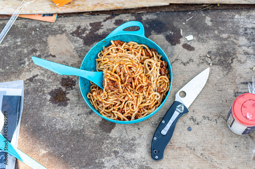 Bolognese pasta in a plate. Cooked pasta with meat. Pasta on a hike. Food for tourists. Tourist lunch. Plate and knife.