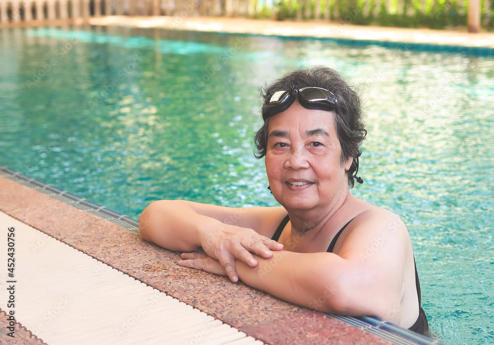 happy and healthy Asian senior woman wearing swim goggles at swimming pool. Fit active senior woman enjoying retirement in swimming pool, smiling and looking at camera.