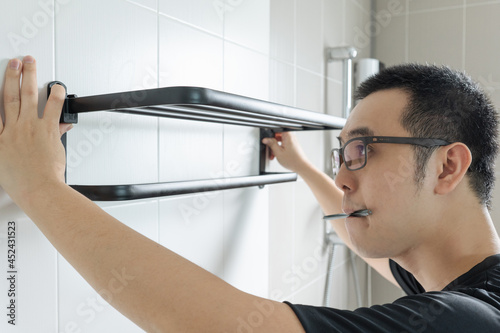 Asian man preparing to install a towel rail on the bathroom wall He put the rack against the wall and used a pencil to mark where to drill.