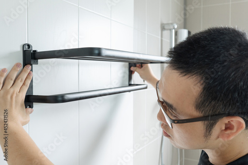 Asian man preparing to install a towel rail on the bathroom wall He put the rack against the wall and used a pencil to mark where to drill.