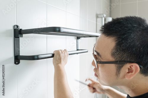 Asian man preparing to install a towel rail on the bathroom wall He put the rack against the wall and used a pencil to mark where to drill.