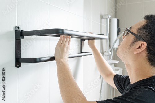 Asian man preparing to install a towel rail on the bathroom wall He put the rack against the wall and used a pencil to mark where to drill.