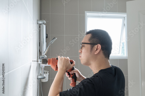 Hard drill - Asian man preparing to install a towel rail on the bathroom wall. He drilled the wall with a drill.