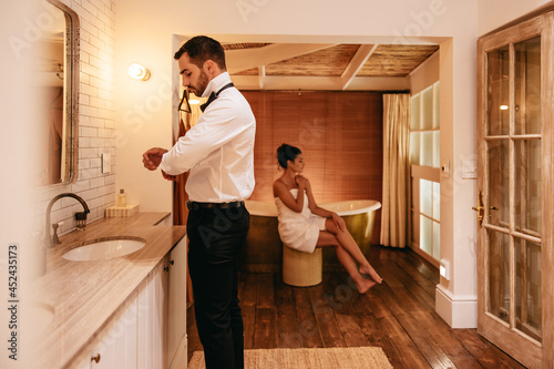 Man getting dressed in a hotel with his wife in the background photo