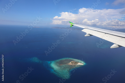 Airplane flying over deep blue sea with an island photo through window plane  © Gatot