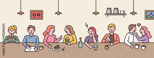 People are chatting while sitting in a row at a table in a cafe.