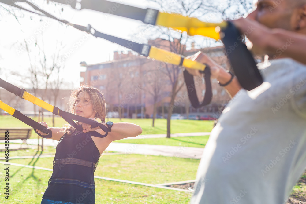 Naklejka premium Fitness couple exercising with fitness straps in the park