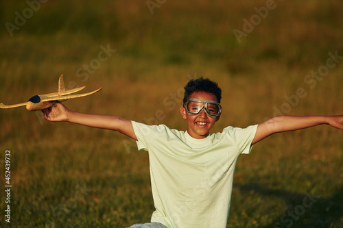 In casual clothes with toy plane. African american kid have fun in the field at summer daytime