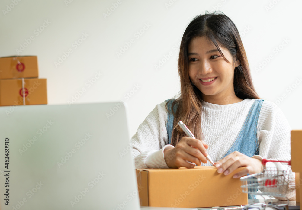 Young smiling beautiful owner asian woman freelance sme business online shopping working on laptop computer with parcel box on desk at home - SME business online and delivery concept Young smiling beautiful owner asian woman freelance sme business online shopping working on laptop computer with parcel box on desk at home - SME business online and delivery concept
