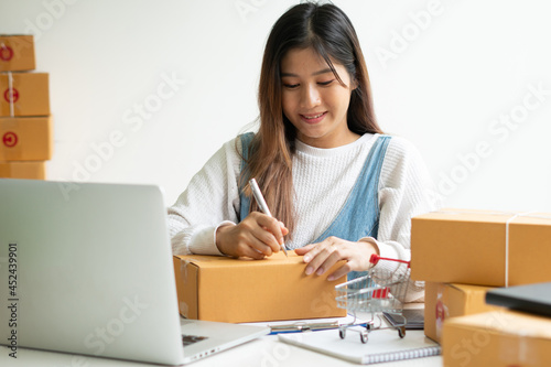 Young smiling beautiful owner asian woman freelance sme business online shopping working on laptop computer with parcel box on desk at home - SME business online and delivery concept © PaeGAG
