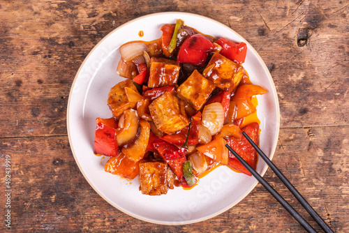 Sweet and sour tofu with peppers and onions in a spicy sauce, serving on a plate with chopsticks, top view. Korean, Chinese and Japanese cuisine.