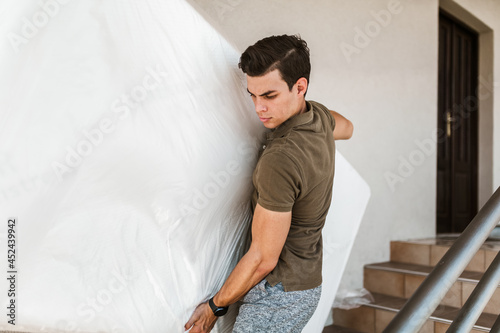 Man carrying the mattress while moving downward the staircase