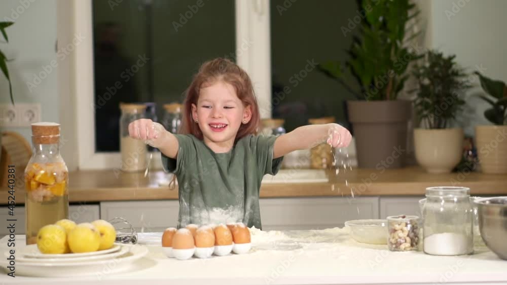 child plays with flour. Little preschool girl learns to prepare dough. Have fun in kitchen with a game. Throw flour splashes in different directions. Clap and laugh. A messy mess. kid stained kitchen. child plays with flour. Little preschool girl learns to prepare dough. Have fun in kitchen with a game. Throw flour splashes in different directions. Clap and laugh. A messy mess. kid stained kitchen.