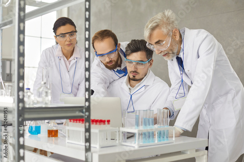 Portrait of a team of scientists working in a modern medical research laboratory. Concentrated serious colleagues discuss and analyze research with a laptop. Concept of science, technology and people