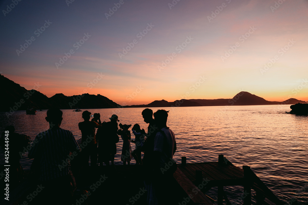 Black silhouette of tourists gathering and doing photoshoot with sea and hills at Labuan Bajo
