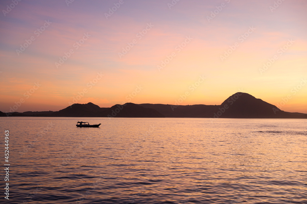 Black silhouette of hills with traditional fishing boat sailing on the sea at Labuan Bajo