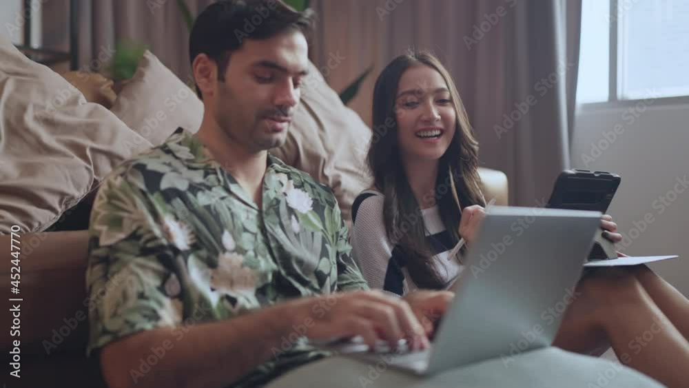 portrait of asian and caucasian marry couple sitting smile relax together on wooden floor in living room at home,marry couple using laptop shopping online together at home