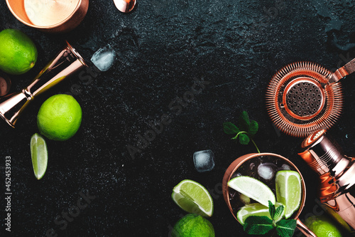 Preparation Moscow Mule cocktail with ginger beer, vodka, lime and ice. Copper bar tools. Black bar counter background. Top view. Copy space
