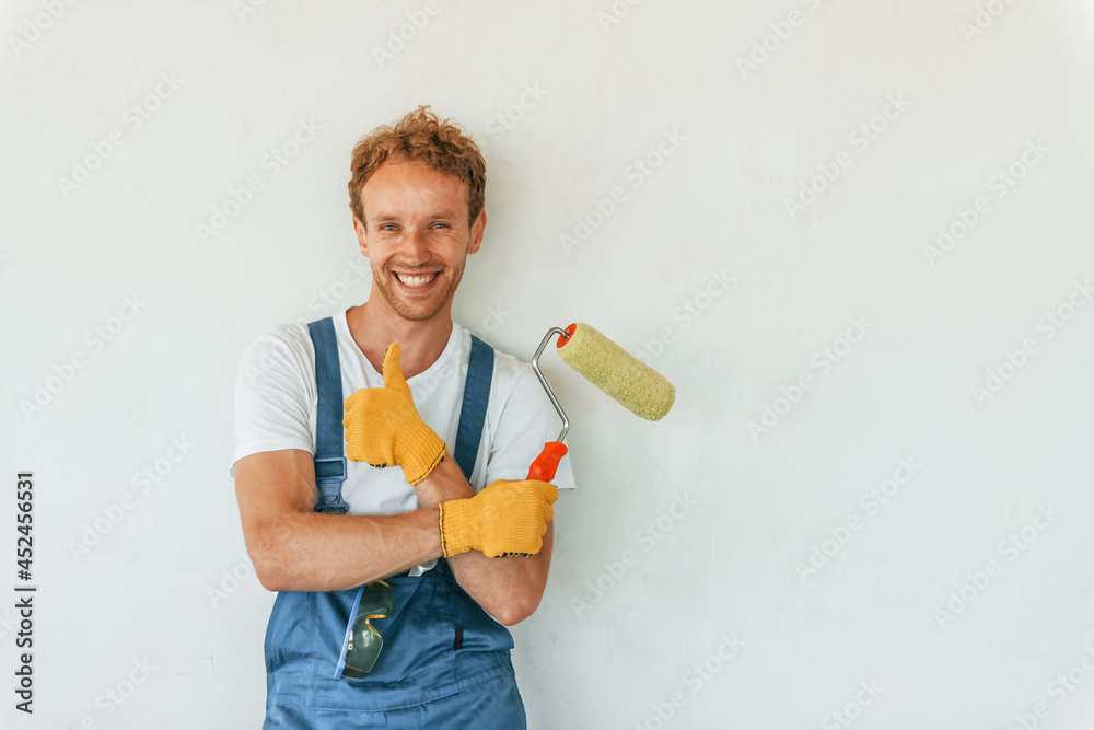 Painting the walls. Young man working in uniform at construction at daytime Painting the walls. Young man working in uniform at construction at daytime