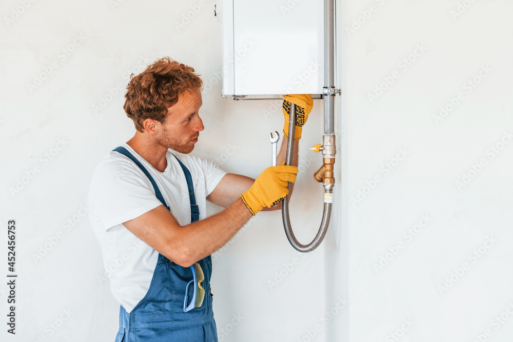 Repairing water heater. Young man working in uniform at construction at daytime Repairing water heater. Young man working in uniform at construction at daytime