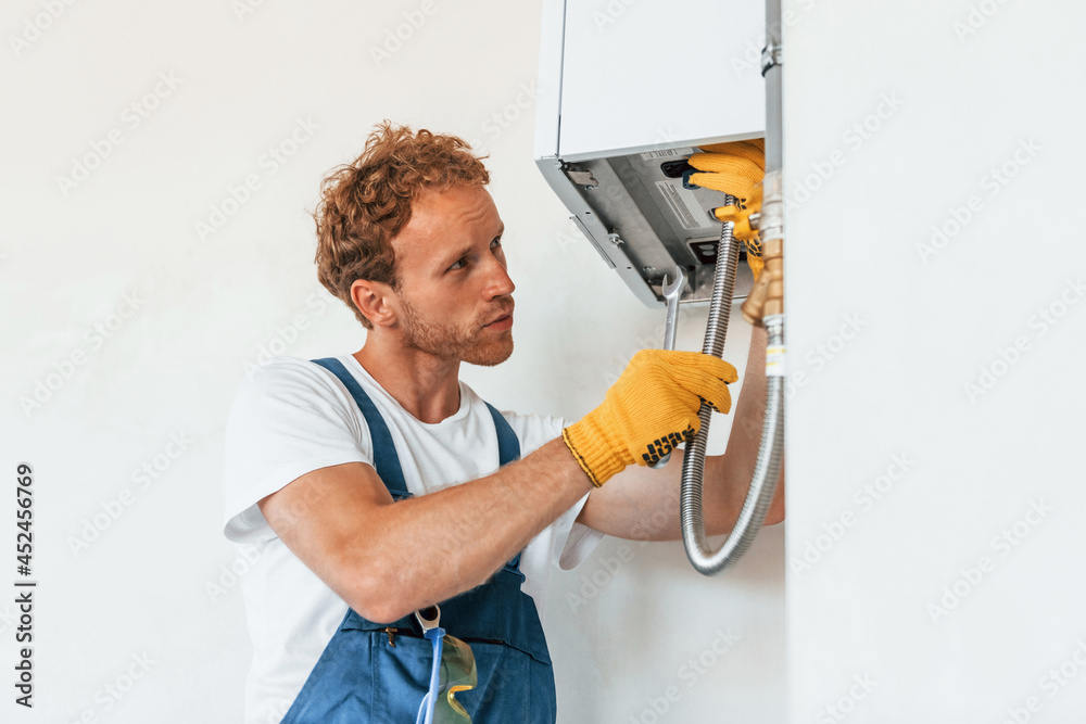 Repairing water heater. Young man working in uniform at construction at daytime Repairing water heater. Young man working in uniform at construction at daytime