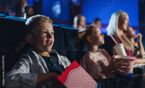 Small boy with family sitting and watching film in the cinema, eating popcorn.