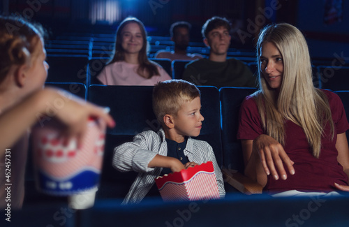 Mother with happy small children in the cinema, watching film and eating popcorn.