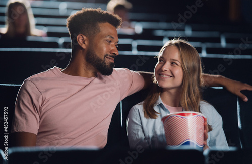 Front view of cheerful young couple in love in the cinema, watching film.