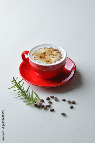Latte coffee in red mug decorated with caramel and chocolate motifs. Coffee beans are part of the composition.