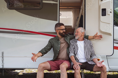 Mature man with senior father sitting by car outdoors, fun on caravan holiday trip.