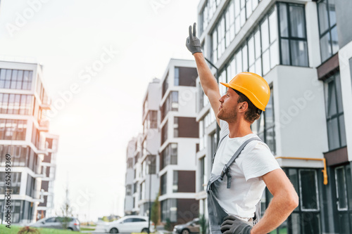 Looking at buildings. Young man working in uniform at construction at daytime