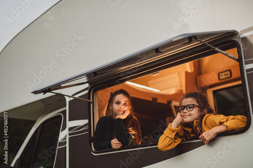 Happy small girls looking out through caravan window in the evening, family holiday trip.