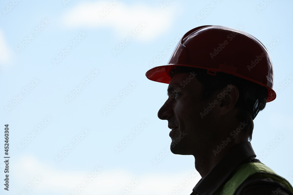 Backlit side view portrait of male construction worker wearing hardhat while standing against sky in background, copy space Backlit side view portrait of male construction worker wearing hardhat while standing against sky in background, copy space