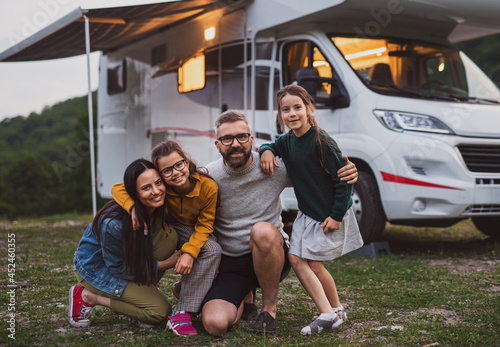 Happy family looking at camera outdoors at dusk, caravan holiday trip.