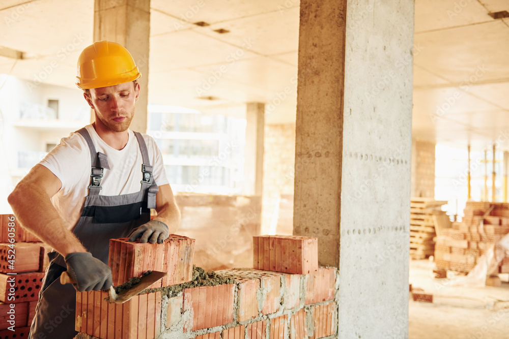 Working by using bricks. Young man in uniform at construction at daytime Working by using bricks. Young man in uniform at construction at daytime
