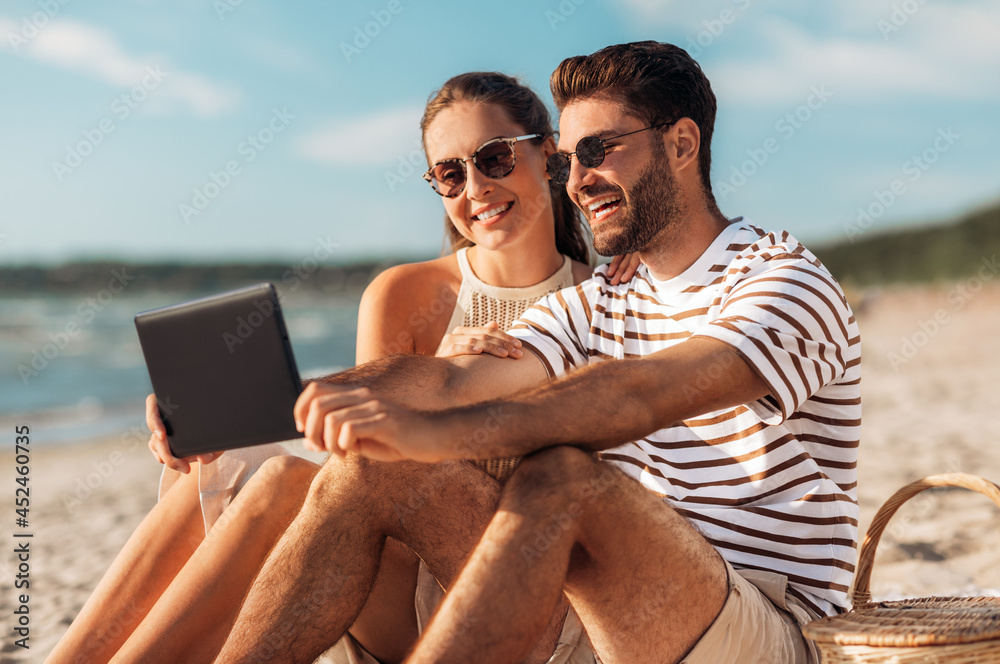 leisure and people concept - happy couple with tablet pc computer and picnic basket on summer beach