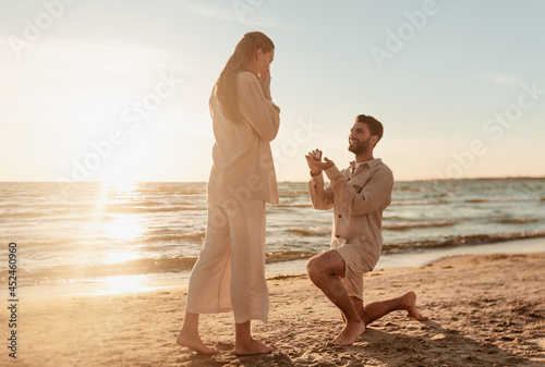 love and people concept - smiling young man with engagement ring making proposal to happy woman on beach photo