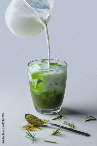 Iced green tea with milk with green tea powder in a small spoon placed next to the glass.