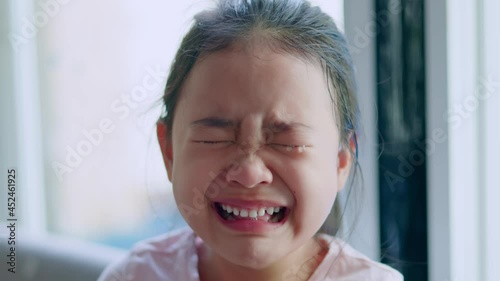 A young Asian girl is crying with tears in her eyes, her mouth wide open and her teeth are white.
