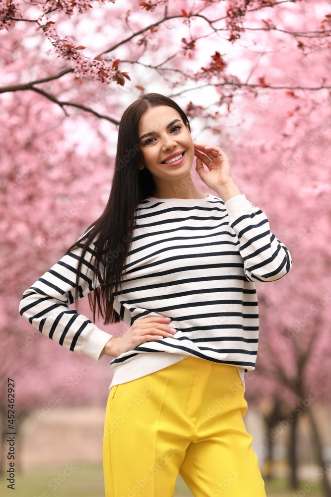 Pretty young woman in park with blooming trees. Spring look Pretty young woman in park with blooming trees. Spring look