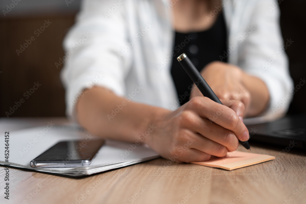Business lady taking notes while working in the office. Woman's hand with a pen close-up. The manager is writing something handwritten at the table. Business and work. Business lady taking notes while working in the office. Woman's hand with a pen close-up. The manager is writing something handwritten at the table. Business and work.
