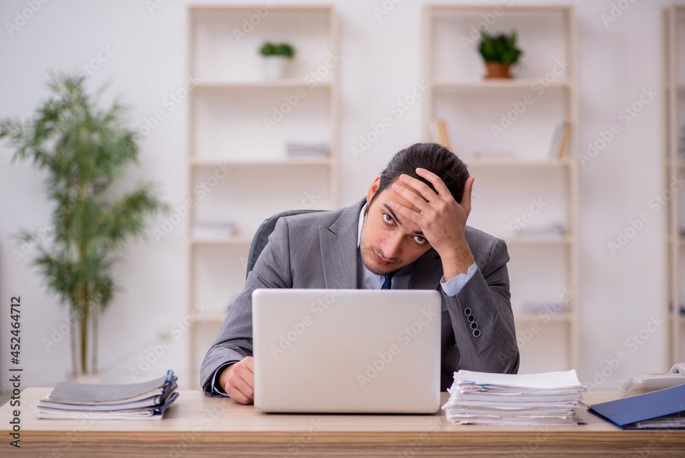 Young male employee unhappy with excessive work in the office Young male employee unhappy with excessive work in the office