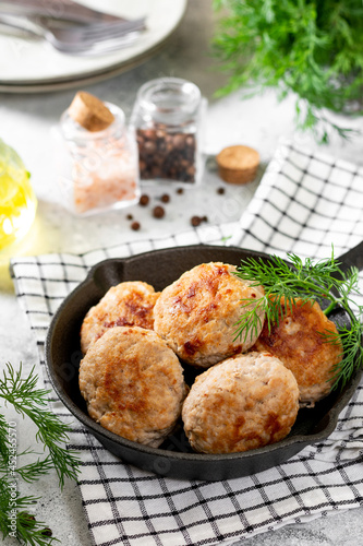 Turkey cutlets in a black frying pan on a light gray cooking table closeup