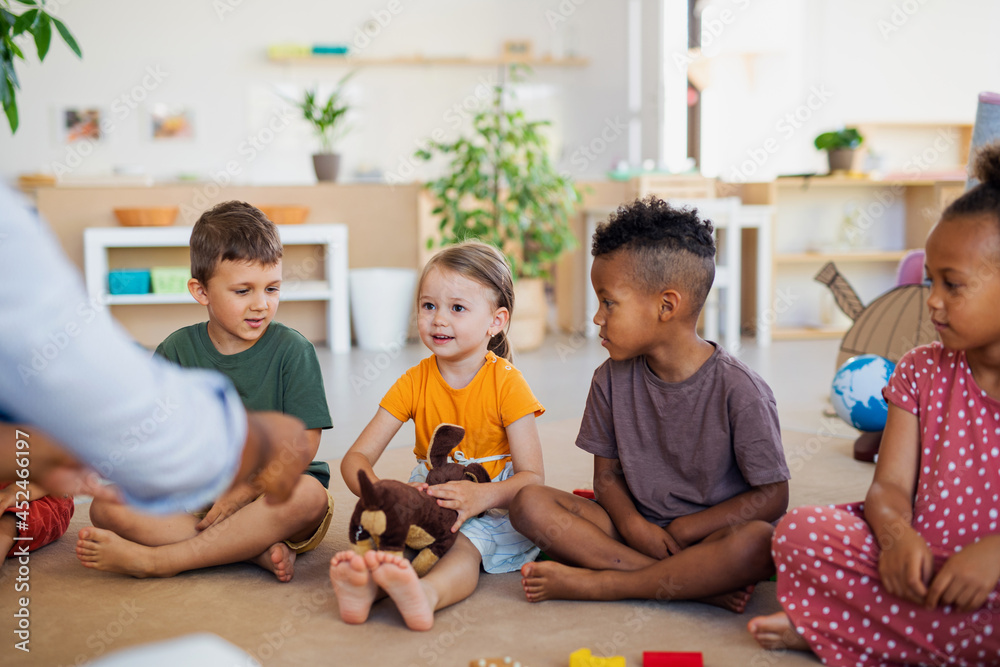 Group of small nursery school children sitting on floor indoors in classroom, listening to teacher. Group of small nursery school children sitting on floor indoors in classroom, listening to teacher.
