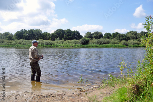 A fisherman is fishing in the river from the bank for spinning.