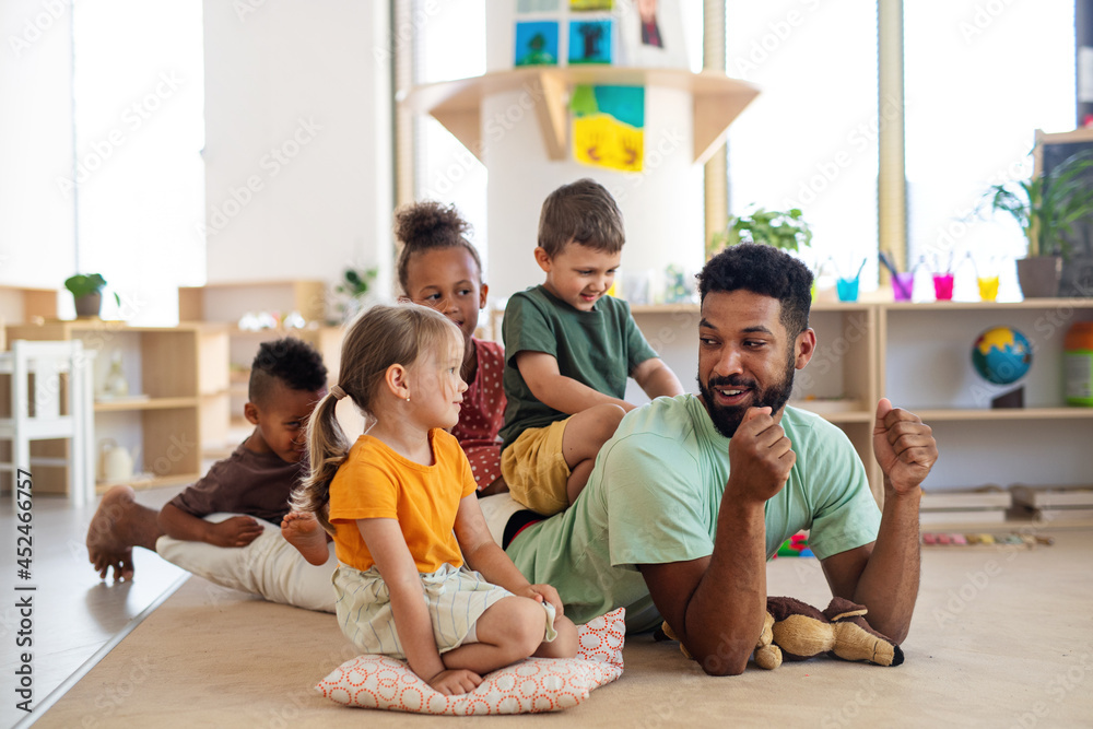 Group of small nursery school children with man teacher sitting on floor indoors in classroom, playing. Group of small nursery school children with man teacher sitting on floor indoors in classroom, playing.
