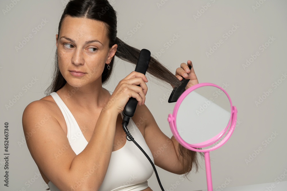 © vladimirfloyd - Young beautiful woman straightening her hair with a straightener © vladimirfloyd - Young beautiful woman straightening her hair with a straightener