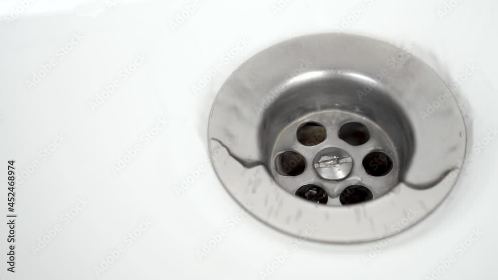 Water splashes and flows into the chrome drain holes of the white bathroom sink. Macro shot. Slow motion Water splashes and flows into the chrome drain holes of the white bathroom sink. Macro shot. Slow motion
