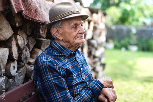 Portrait of elderly man sitting on bench outdoors in garden, resting.