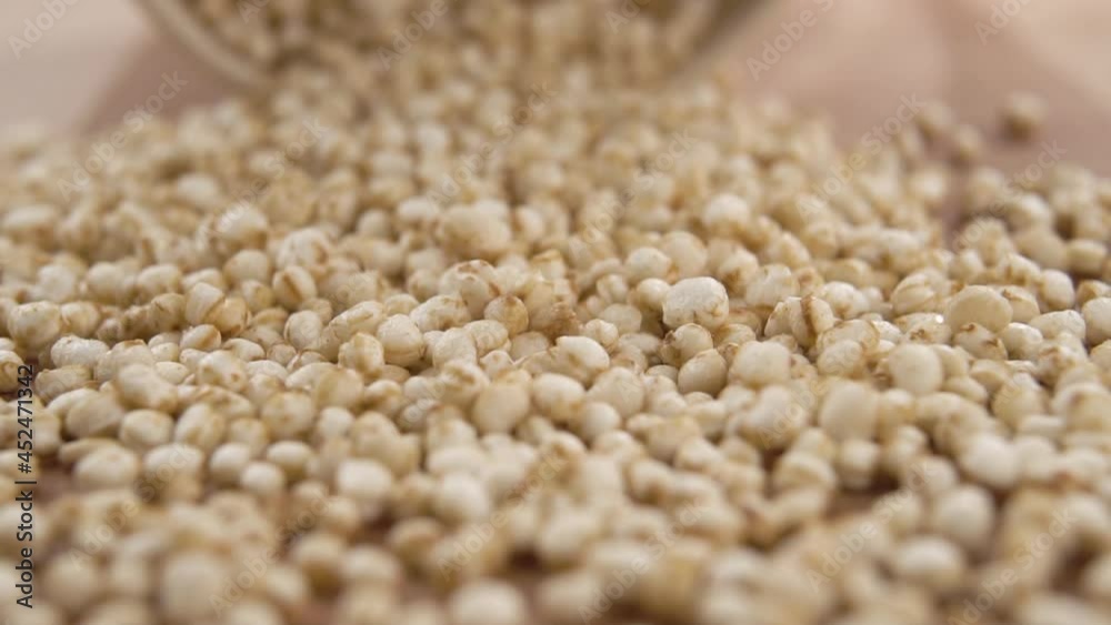 Puffy dry uncooked quinoa falls with paper cup and scatters on a wooden surface. Macro. Slow motion. Gluten free healthy food concept. Selective focus Puffy dry uncooked quinoa falls with paper cup and scatters on a wooden surface. Macro. Slow motion. Gluten free healthy food concept. Selective focus